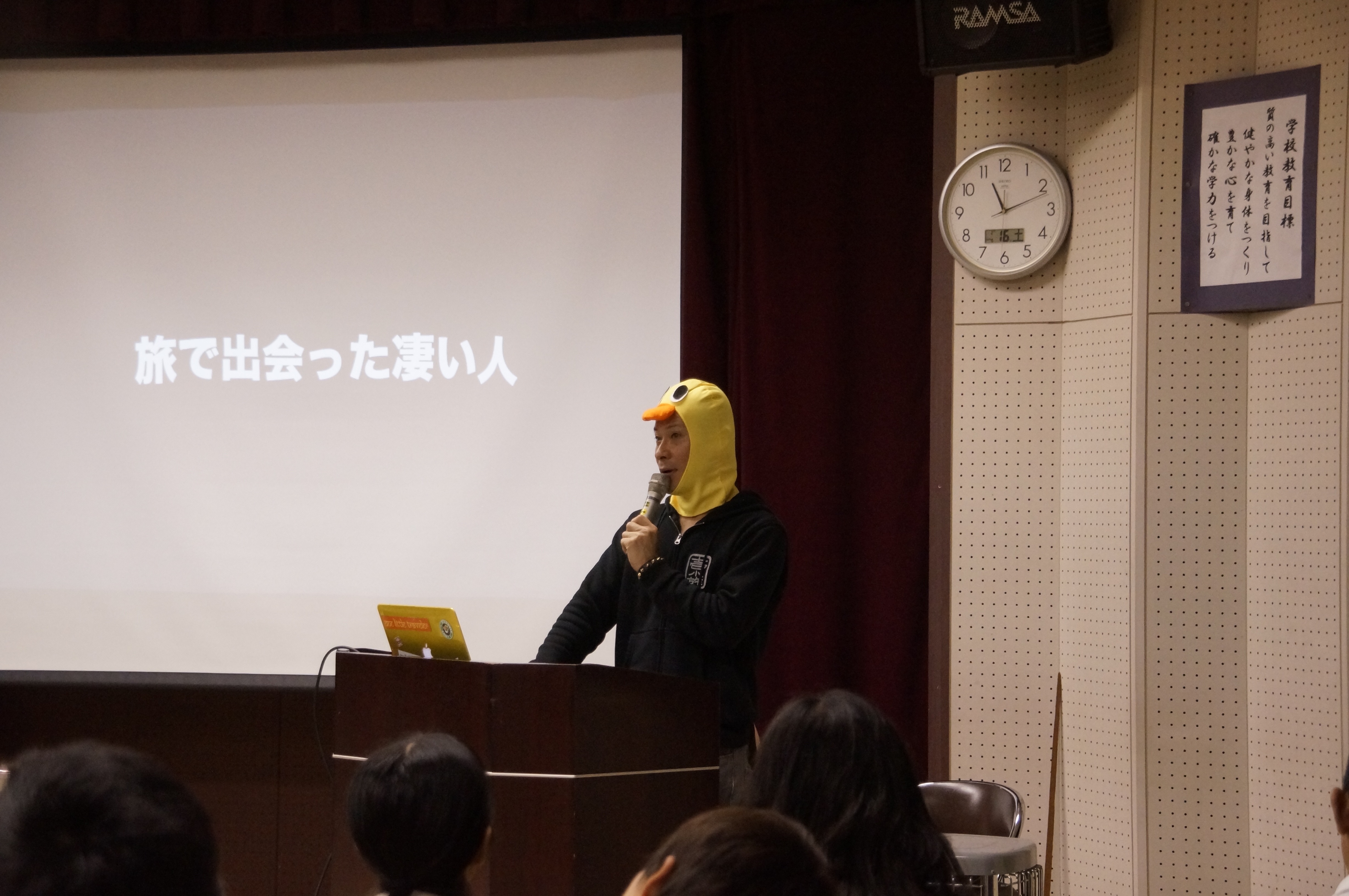 過去の講演で、アヒルの被り物を着け、旅の出会いについてマイクで話すスターダックトニー